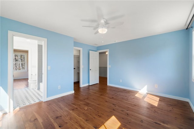 unfurnished bedroom with a walk in closet, baseboards, and wood finished floors