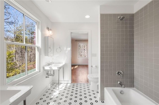 bathroom featuring toilet, a healthy amount of sunlight, bathtub / shower combination, and baseboards