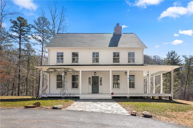 view of front facade featuring roof with shingles, a porch, a chimney, and a front lawn