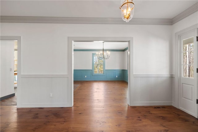 unfurnished dining area featuring hardwood / wood-style flooring, wainscoting, crown molding, and an inviting chandelier