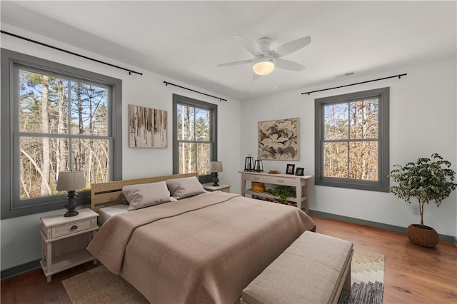bedroom with a ceiling fan, visible vents, wood finished floors, and baseboards