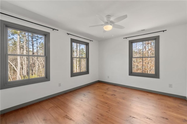 empty room with hardwood / wood-style flooring, a ceiling fan, visible vents, and baseboards