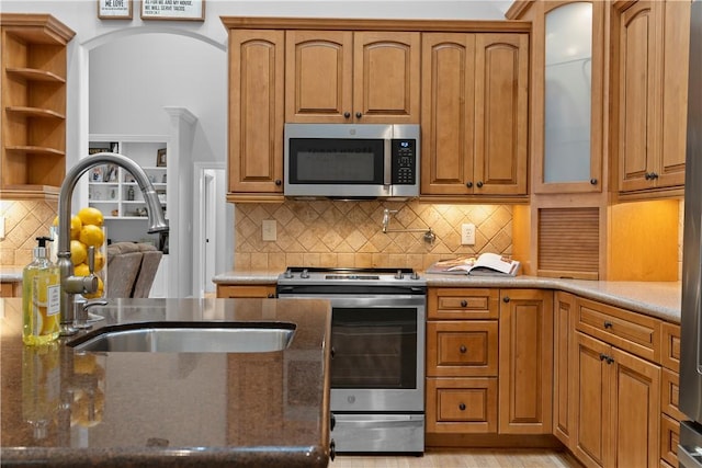 kitchen featuring stainless steel appliances, dark stone countertops, a sink, and glass insert cabinets