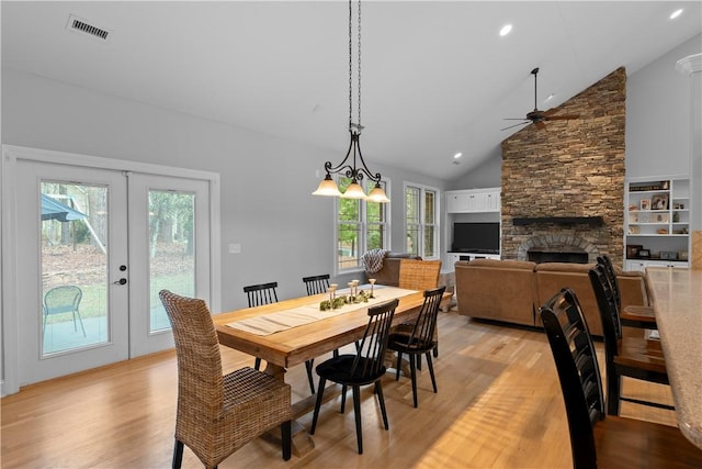 dining space with light wood-type flooring, french doors, visible vents, and a fireplace