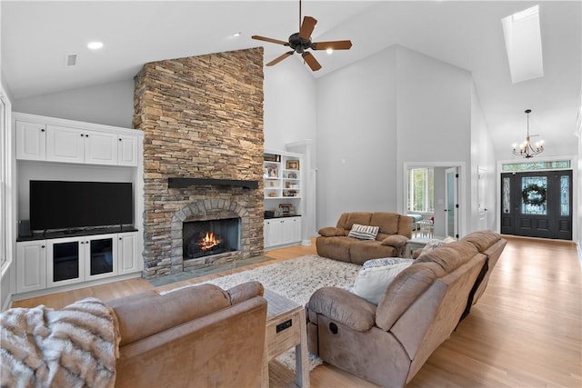 living room with ceiling fan with notable chandelier, a stone fireplace, light wood finished floors, and high vaulted ceiling