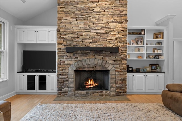 living area with lofted ceiling, light wood-style flooring, and a stone fireplace