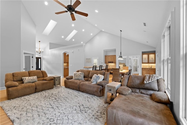 living area featuring high vaulted ceiling, ceiling fan with notable chandelier, a skylight, wood finished floors, and visible vents