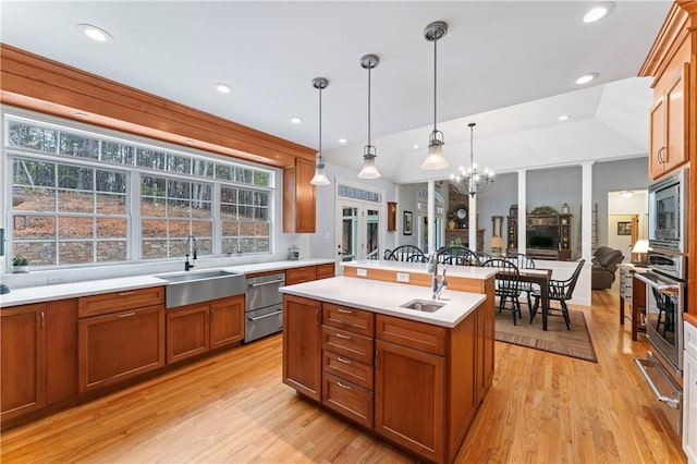 kitchen with brown cabinetry, an island with sink, stainless steel appliances, light countertops, and a sink