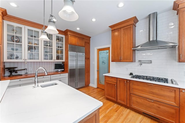 kitchen with light countertops, stainless steel built in fridge, a sink, gas cooktop, and wall chimney exhaust hood