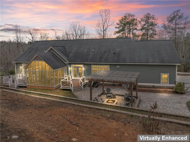 back of property at dusk with roof with shingles and a patio area