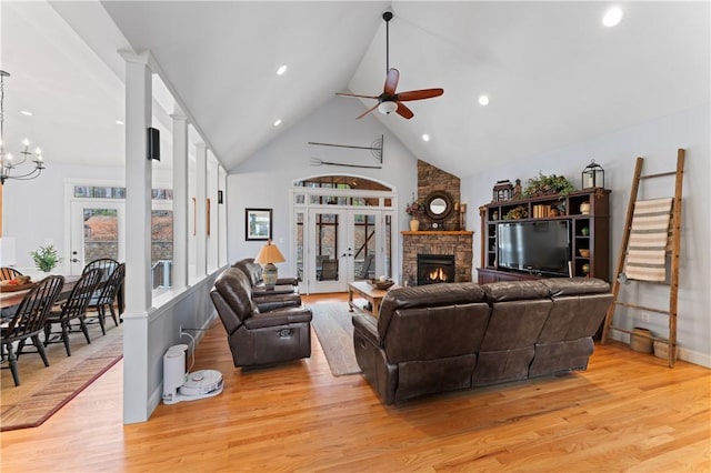 living room with high vaulted ceiling, a fireplace, light wood finished floors, and ceiling fan with notable chandelier