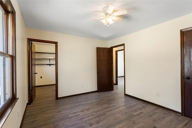 unfurnished bedroom with wood finished floors, a ceiling fan, baseboards, a spacious closet, and a closet