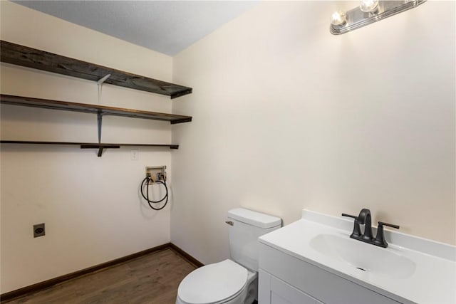 half bath featuring toilet, baseboards, wood finished floors, and vanity