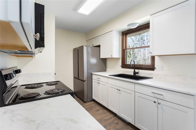 kitchen featuring light stone counters, electric range, freestanding refrigerator, white cabinets, and a sink