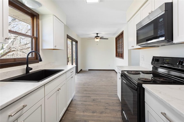 kitchen featuring white cabinets, stainless steel microwave, a sink, and black / electric stove