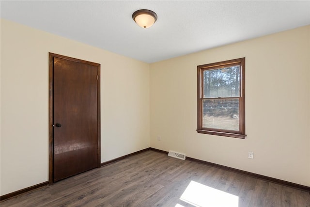 empty room with dark wood-style floors, visible vents, and baseboards