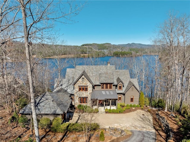 view of front of house featuring a water view, dirt driveway, stone siding, a chimney, and a high end roof