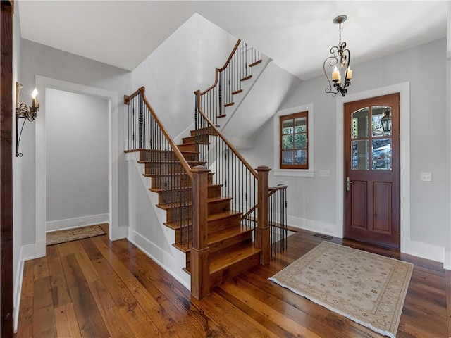 entrance foyer featuring visible vents, baseboards, wood-type flooring, stairway, and a chandelier