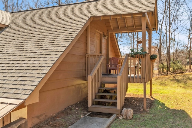 property entrance with a wooden deck, a lawn, and roof with shingles