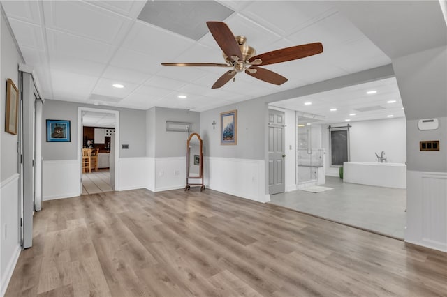 unfurnished living room featuring light wood-type flooring, a barn door, and wainscoting