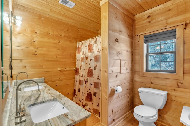 bathroom with toilet, wooden walls, visible vents, and a sink