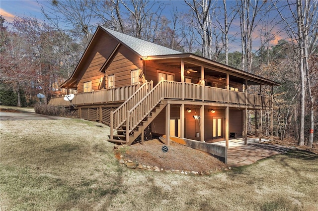 view of front of home with a shingled roof, a ceiling fan, stairway, a wooden deck, and a front yard