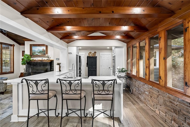 kitchen featuring vaulted ceiling with beams, light countertops, freestanding refrigerator, wood ceiling, and a peninsula