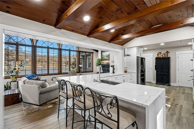 kitchen featuring white cabinets, lofted ceiling with beams, light stone counters, freestanding refrigerator, and a sink