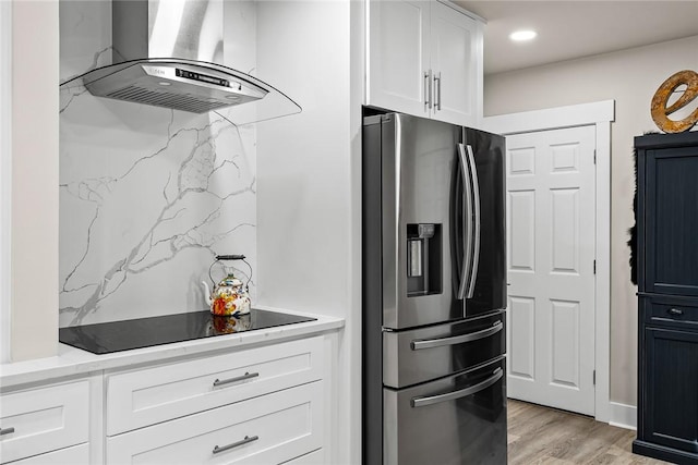 kitchen featuring white cabinets, wall chimney exhaust hood, light wood-style floors, stainless steel refrigerator with ice dispenser, and recessed lighting