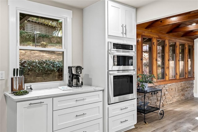 kitchen featuring double oven, light wood finished floors, light stone countertops, and white cabinets