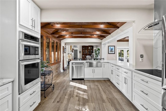 kitchen featuring beam ceiling, light wood finished floors, appliances with stainless steel finishes, white cabinetry, and a sink