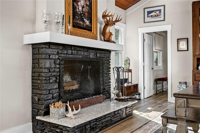 living area featuring lofted ceiling, a fireplace with raised hearth, baseboards, and wood finished floors