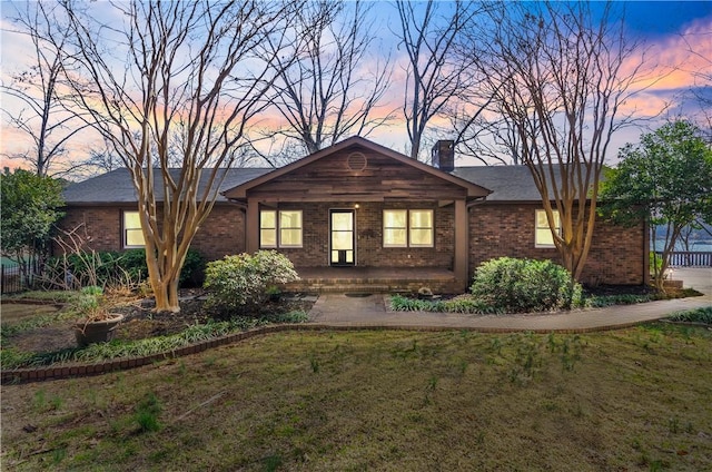 ranch-style home with a front yard, a chimney, a porch, and brick siding