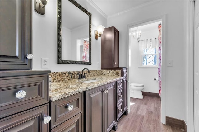 bathroom featuring toilet, wood finished floors, vanity, baseboards, and ornamental molding