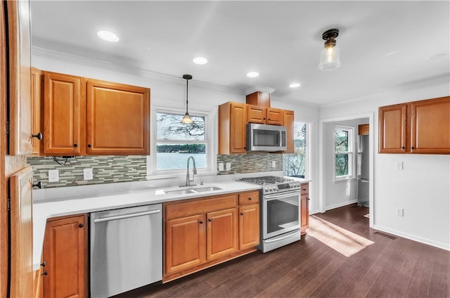 kitchen with stainless steel appliances, a sink, light countertops, ornamental molding, and dark wood-style floors