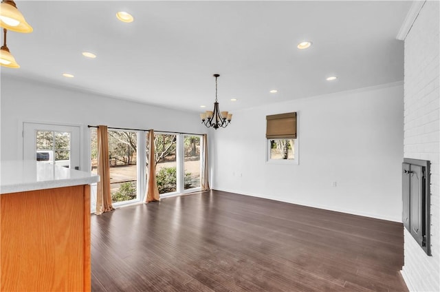 unfurnished living room featuring dark wood-style floors, a brick fireplace, a chandelier, and recessed lighting