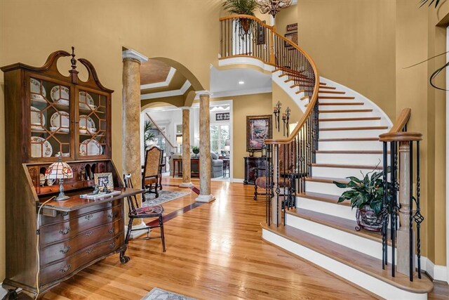 foyer entrance featuring arched walkways, light wood-style flooring, stairway, crown molding, and ornate columns