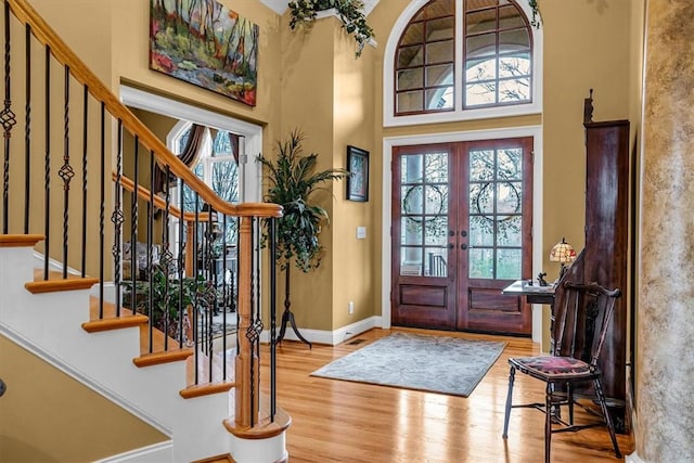 foyer entrance with baseboards, wood finished floors, stairs, a high ceiling, and french doors