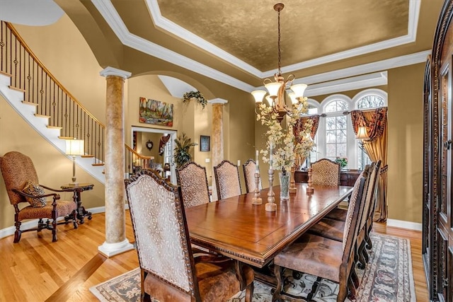 dining space with ornate columns, crown molding, a tray ceiling, and wood finished floors