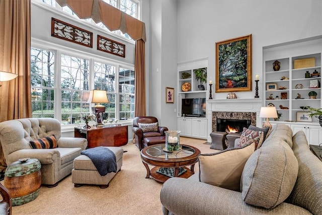 sitting room featuring built in features, a high end fireplace, a towering ceiling, and carpet