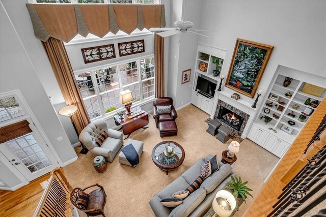 living area with baseboards, a towering ceiling, carpet floors, built in shelves, and a fireplace