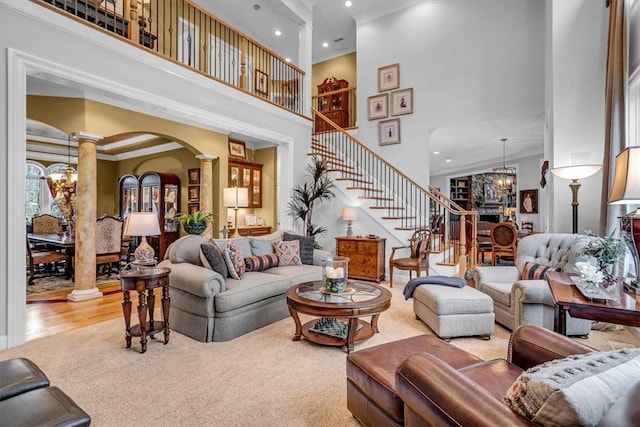 living area featuring a towering ceiling, stairway, ornamental molding, a chandelier, and ornate columns