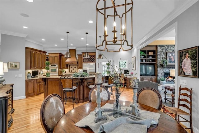 dining area featuring light wood-style flooring, recessed lighting, a fireplace, baseboards, and crown molding