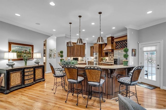 kitchen with light wood-style flooring, appliances with stainless steel finishes, hanging light fixtures, custom exhaust hood, and a kitchen bar