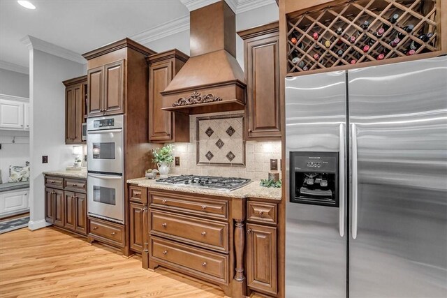 kitchen featuring light wood-style flooring, stainless steel appliances, ornamental molding, decorative backsplash, and custom range hood