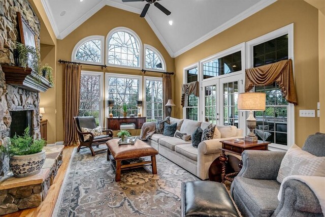 sunroom featuring a ceiling fan, vaulted ceiling, french doors, and a stone fireplace