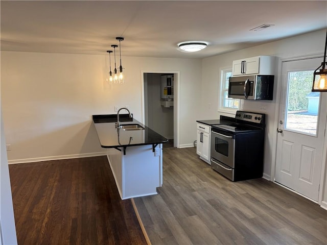 kitchen featuring stainless steel appliances, dark countertops, visible vents, a sink, and a peninsula