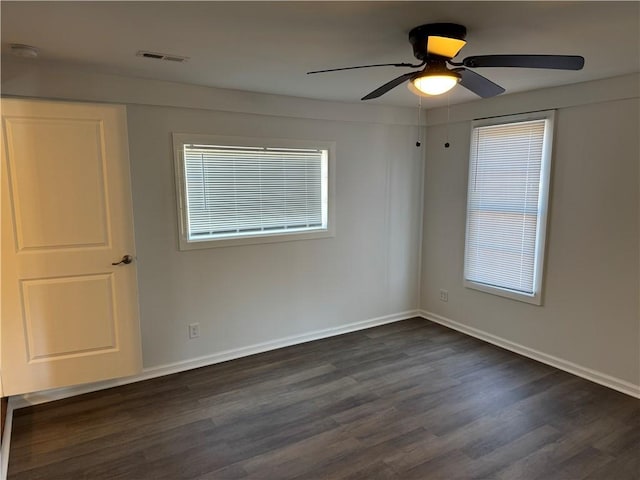 empty room featuring ceiling fan, dark wood-style flooring, visible vents, and baseboards