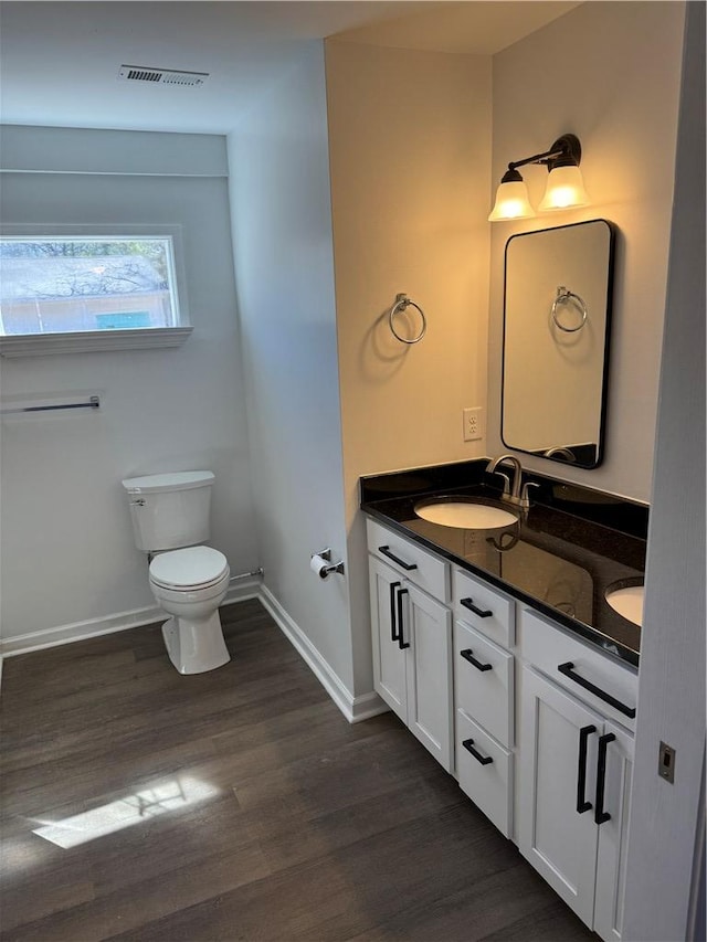 bathroom with toilet, wood finished floors, a sink, baseboards, and double vanity