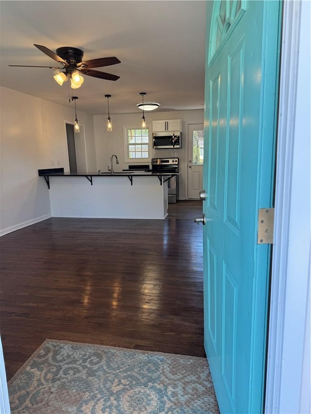 interior space featuring white cabinets, dark countertops, dark wood-style floors, appliances with stainless steel finishes, and a breakfast bar area